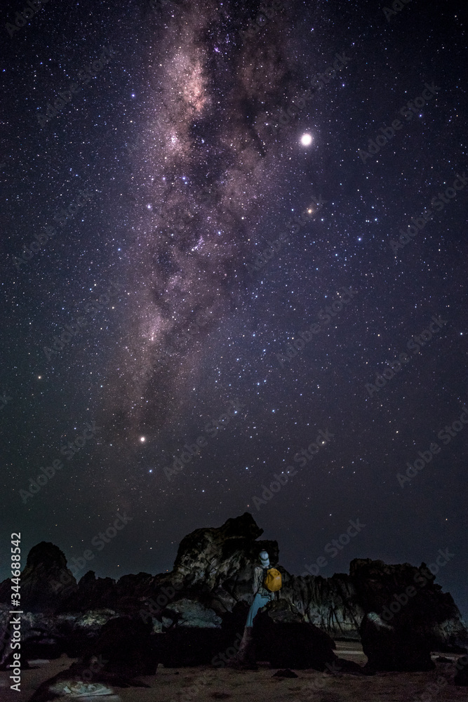 Person enjoys amazing magical milky way galaxy night sky nearby rock formations at the beach
