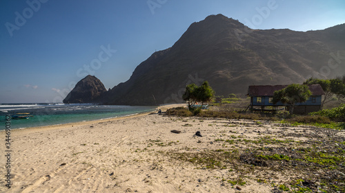 Local fisherman sitting on a shade at nice clean beach big headland hill beyond and wooden house  boats nearby. Sumbawa