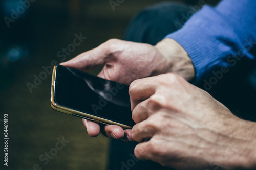 Man using a smartphone and scrolling by using both hands. Male holding a mobile phone, close up, dark tone, selective focus.