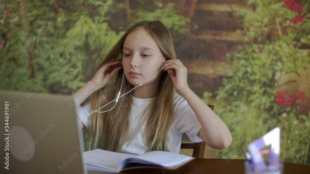 Focused young girl wearing earphones and looking at laptop. Cheerful schoolgirl communicating via laptop. Communication, technology concept Focused young girl wearing earphones and looking at laptop. Cheerful schoolgirl communicating via laptop. Communication, technology concept