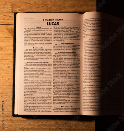 Bíblia Sagrada em cima de uma mesa e debaixo de uma luminária em um quarto escuro.
