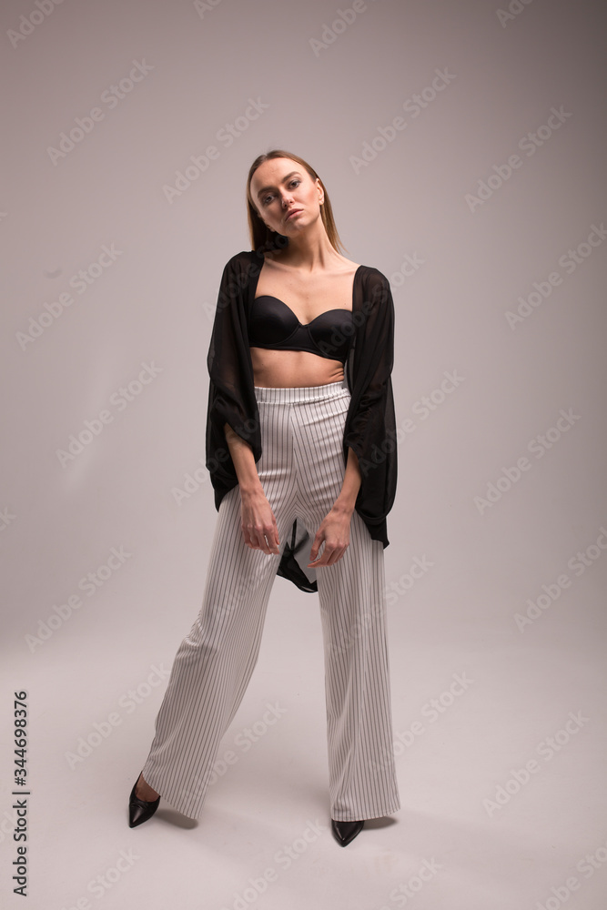 fashion look girl in pants with stripes and black top on plane studio background, supermodel posing, copy space fashion look girl in pants with stripes and black top on plane studio background, supermodel posing, copy space