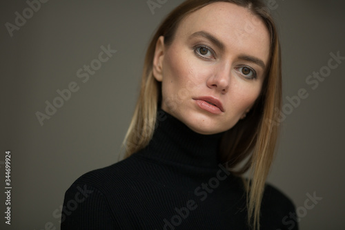 close up portrait of stylish looking girl in black turtleneck with blue eyes, model posing in interior, studio background 