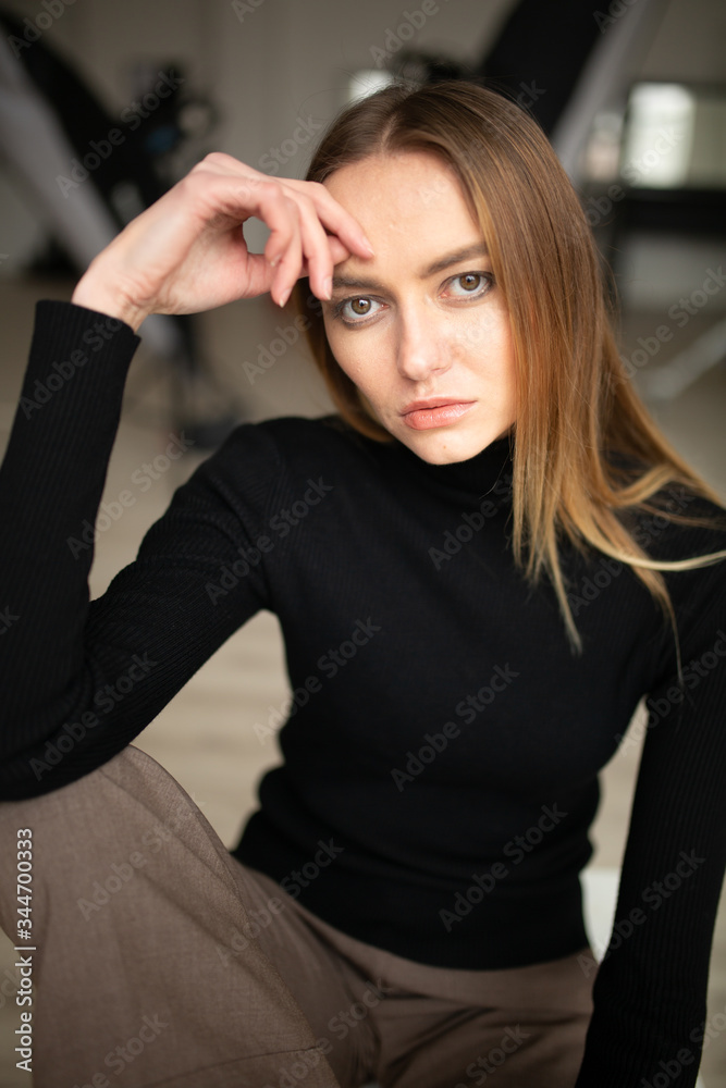 close up portrait of stylish looking girl in black turtleneck with blue eyes, model posing in interior, studio background 