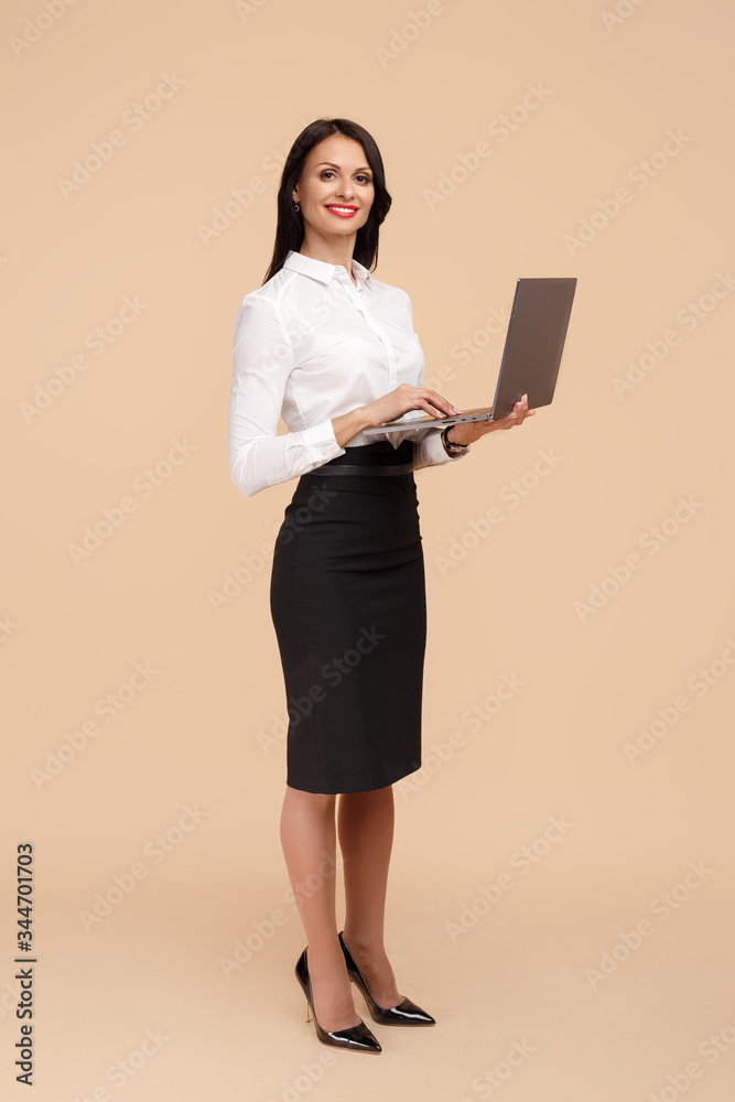 Fototapeta premium Full lengh photo of happy young modern business woman over beige background, working on laptop computer.