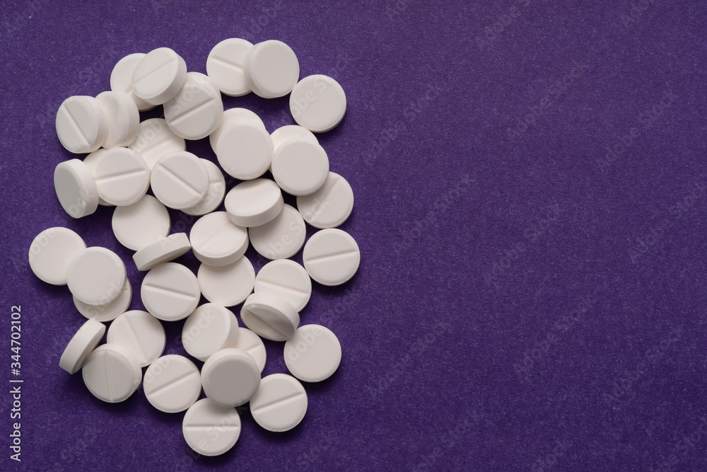 White tablets are scattered from a bottle on a purple background.