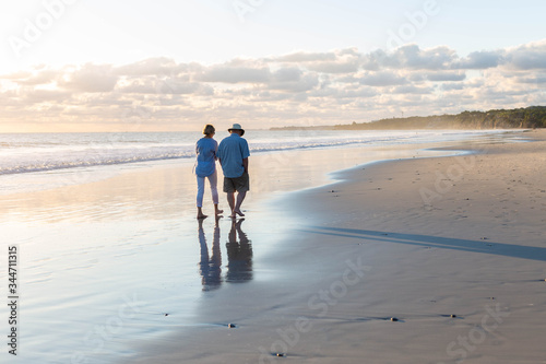 Pareja caminando por espejo de agua en una playa tranquila papa e hija mayor  photo