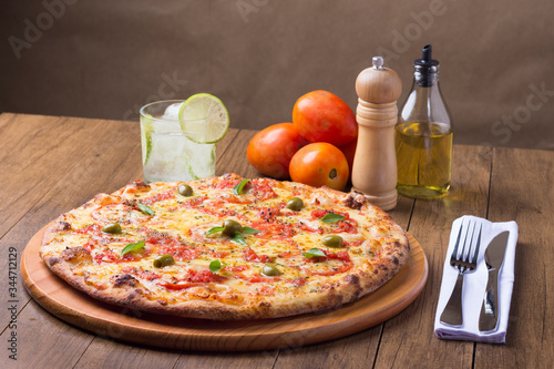 Pizza Marguerita made with tasty pizza dough, Mozzarella, tomatoes, marjoram and green olives. On the wooden board. Napolitan Pizza. Sparkling water Lemon and ice cubes. Fork and knife. Photo  photo
