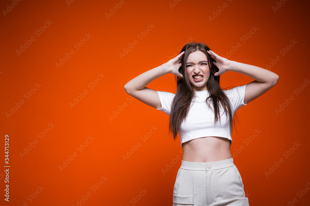The girl growls and grins in a white t-shirt holds her head in her hands, ruffling her long hair. Orange background, concept sales The girl growls and grins in a white t-shirt holds her head in her hands, ruffling her long hair. Orange background, concept sales