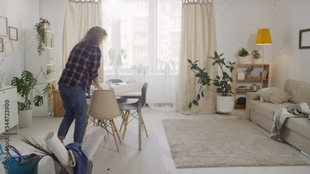 Timelapse of young woman entering frame and cleaning messy apartment: she is picking up papers, cleaning surfaces and mopping floor