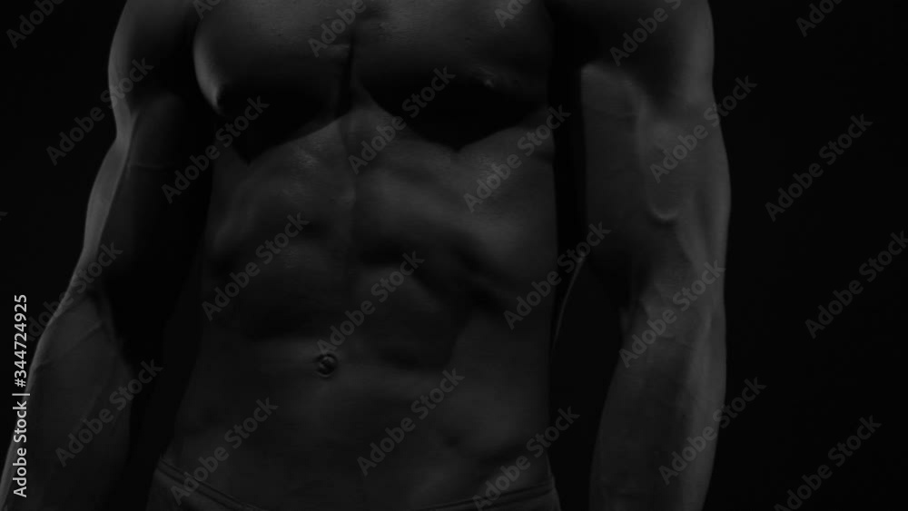 Strong bodybuilder posing and training in contrast light showing his body and every muscle on it under water drops and slow rain Strong bodybuilder posing and training in contrast light showing his body and every muscle on it under water drops and slow rain