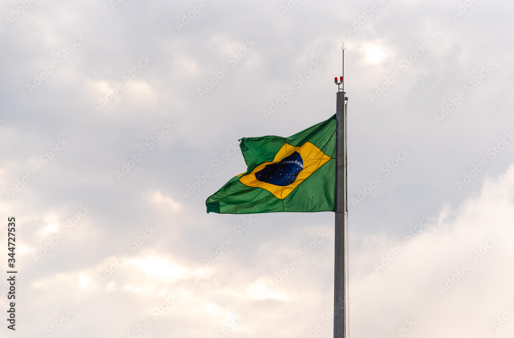 Flag of Brazil fluttering in the wind hoisted on iron mast on light and outdoors background Flag of Brazil fluttering in the wind hoisted on iron mast on light and outdoors background