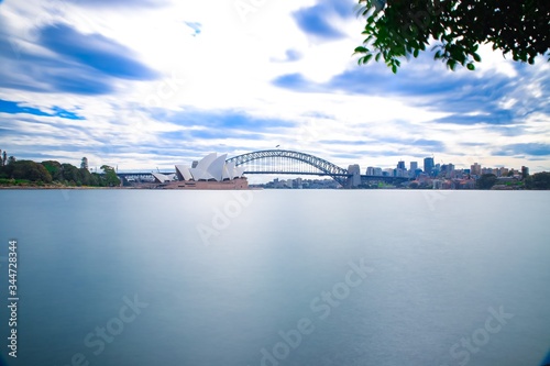 Long exposure on a partly cloudy afternoon on Sydney Harbour with nice rocks in the foreground the soft waves crashing on the shore and the beautiful harbour foreshore as a backdrop