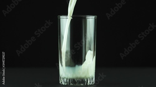 Milk pouring into glass close up isolated on black background Slow motion . Milk is holesome and natural product for healthy lifestyle photo