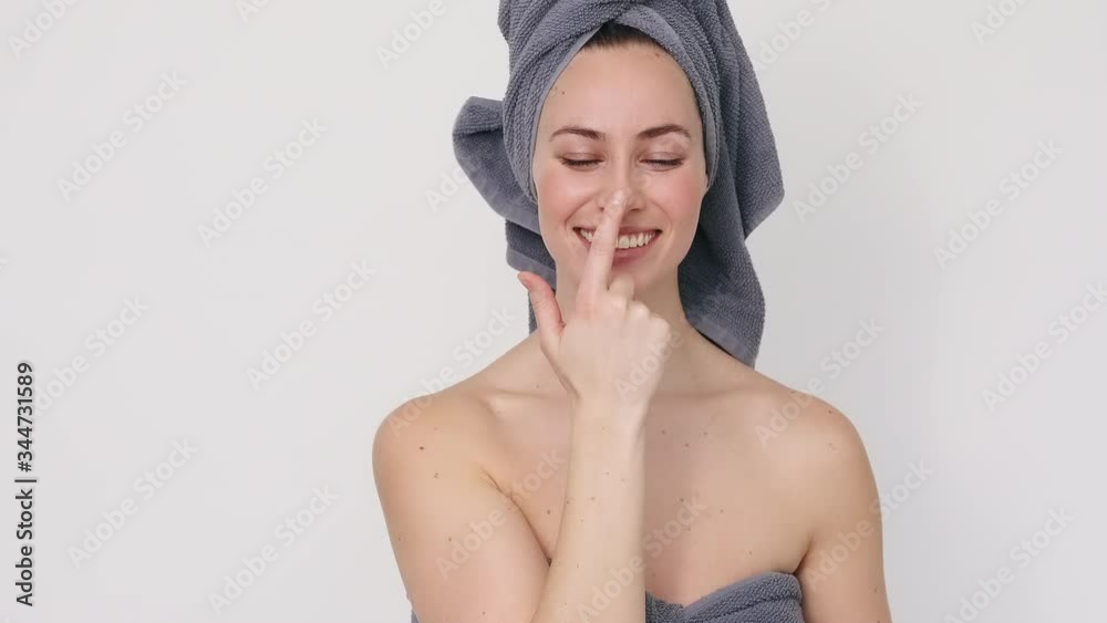 Young and healthy woman with perfect skin, wearing a towel, applying moisturizing cream on her nose and posing after. It's a fun way to show wellness and beauty products.  