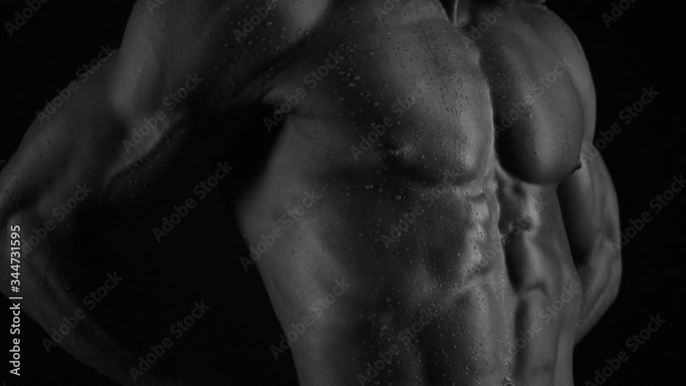 Strong bodybuilder posing and training in contrast light showing his body and every muscle on it under water drops and slow rain Strong bodybuilder posing and training in contrast light showing his body and every muscle on it under water drops and slow rain