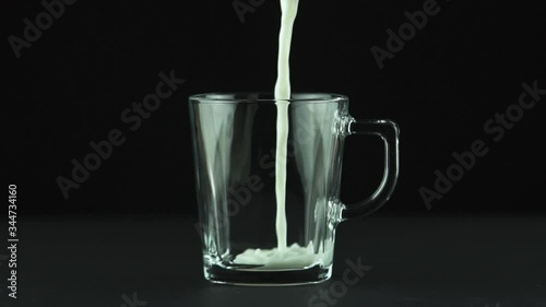 Milk pouring into glass mug close up isolated on black background Slow motion . Milk is holesome and natural product for healthy lifestyle photo