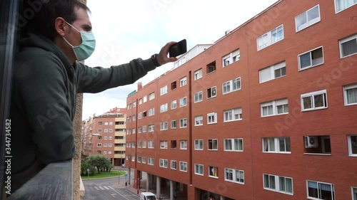 sick man covid-19 virus with mask peeking out the window using a smartphone