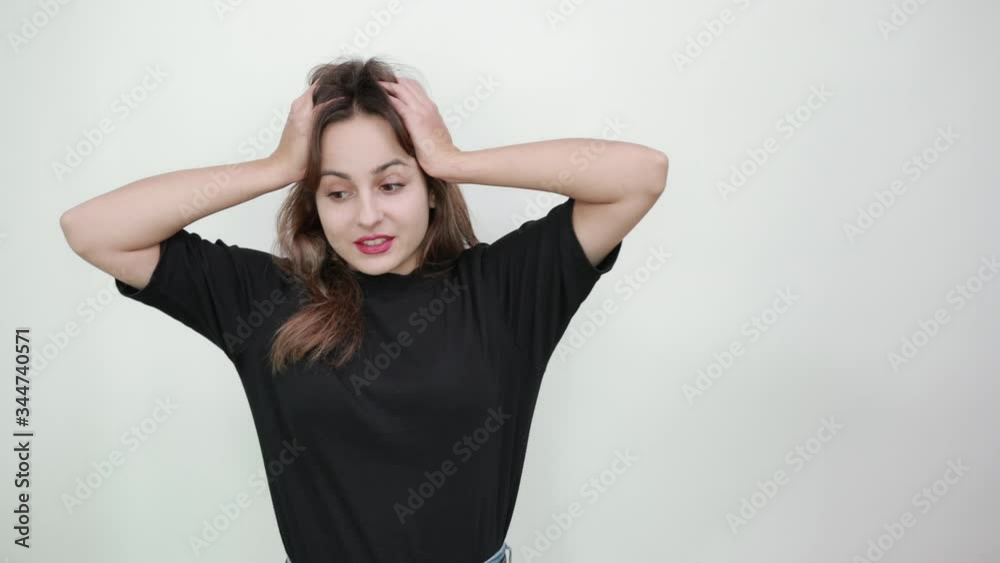 Cute Young Brunette Woman In Black T-Shirt, Blue Jeans With Belt On Gray Background, A Disappointed Girl Is Confused With Her Hands On Head And Thinks What To Do