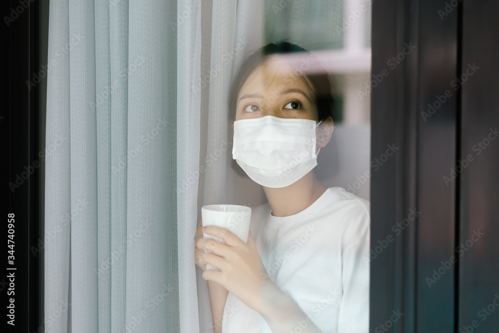 Sick asian female of corona virus looking through the window and wearing mask protection and recovery from the illness in home. Quarantine. Patient isolated to prevent infection. Sick asian female of corona virus looking through the window and wearing mask protection and recovery from the illness in home. Quarantine. Patient isolated to prevent infection.