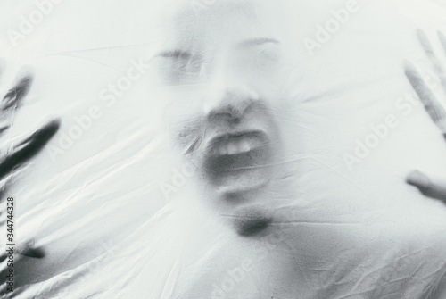 Beautiful female face through the fabric. Scary black and white background photo