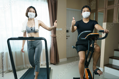 Exercise at home: man biking exercise or Indoor cycling and woman running on a treadmill with mask : health care during Coronavirus pandemic.