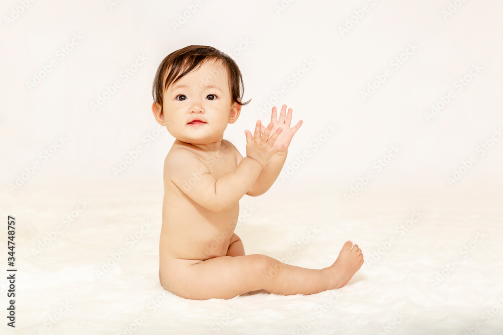 白背景を前に裸で座り手を叩く女の子の赤ちゃん 白背景を前に裸で座り手を叩く女の子の赤ちゃん