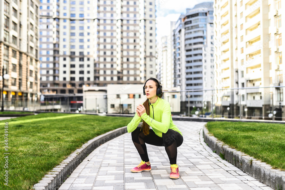 A young woman in sportswear is warming up before outdoors workout among skyscrapers. She doing sit-ups and listening music in headphones. Healthy lifestyle
