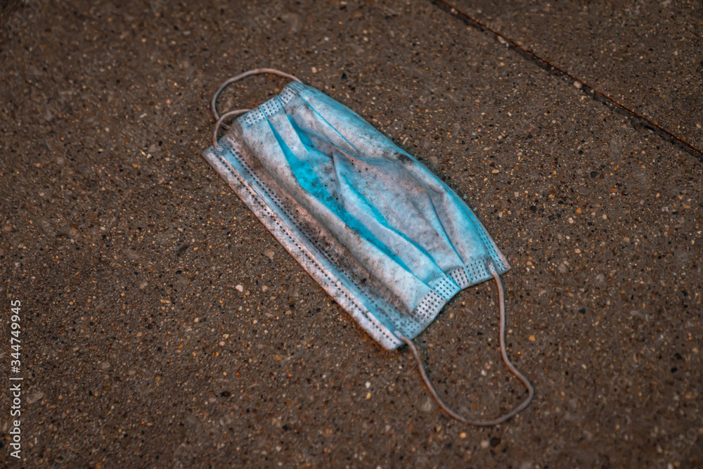 A close up of a lost, discarded or dropped blue single worn, dirty and wet face mask or surgical doctor or nurse mask with elastic bands littering the sidewalk or concrete pavement in downtown Chicago A close up of a lost, discarded or dropped blue single worn, dirty and wet face mask or surgical doctor or nurse mask with elastic bands littering the sidewalk or concrete pavement in downtown Chicago