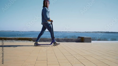 Young asian woman in a jeans jacket walks with the scooter near the river photo