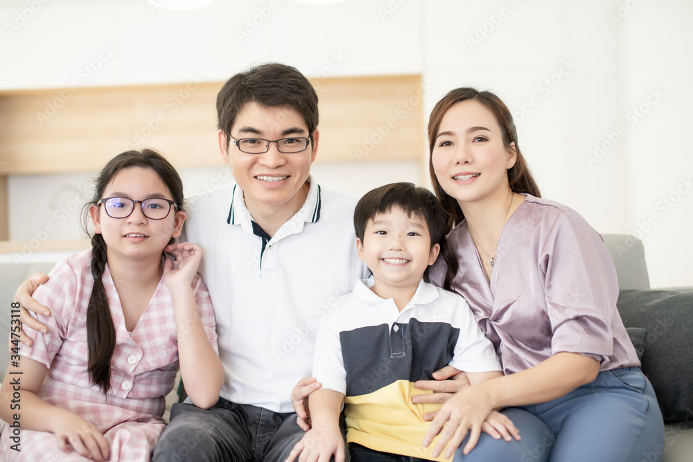 Asian family wear glasses happy smile portrait sitting in gray sofa with kitchen room in background, parent and kid is real people family. Asian family wear glasses happy smile portrait sitting in gray sofa with kitchen room in background, parent and kid is real people family.