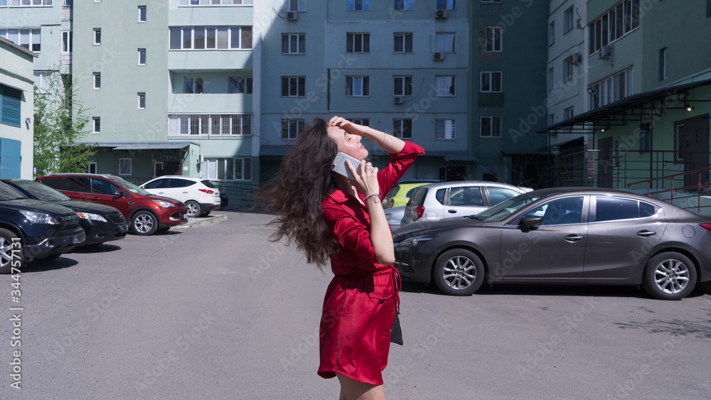 Beautiful attractive brunette young woman in red dress talking on phone along.Busy trendy girl on street near buidings.