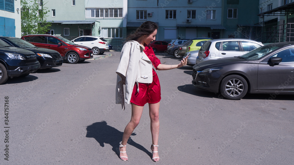 Emotional young beautiful woman walking on street on white
 high heels shoes and red dress.Beautiful brunette woman in shock with open mouth looking on phone.