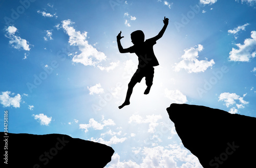 Happy silhouette of boy jumps over a cliff.