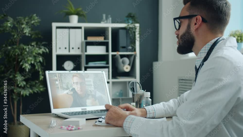 Young man doctor is giving medical advice to unhealthy guy during internet consultation using laptop computer in hospital talking discussing treatment and diagnosis. Young man doctor is giving medical advice to unhealthy guy during internet consultation using laptop computer in hospital talking discussing treatment and diagnosis.