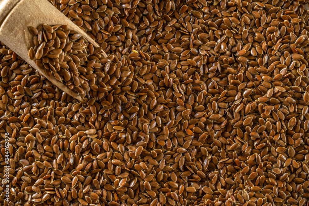 Linen seed, flaxseed - organic food background. Brown flax, linseed in wooden scoop for oil isolated dark stone. Vegan sources of omega 3 and unsaturated fats. Concept of healthy food.