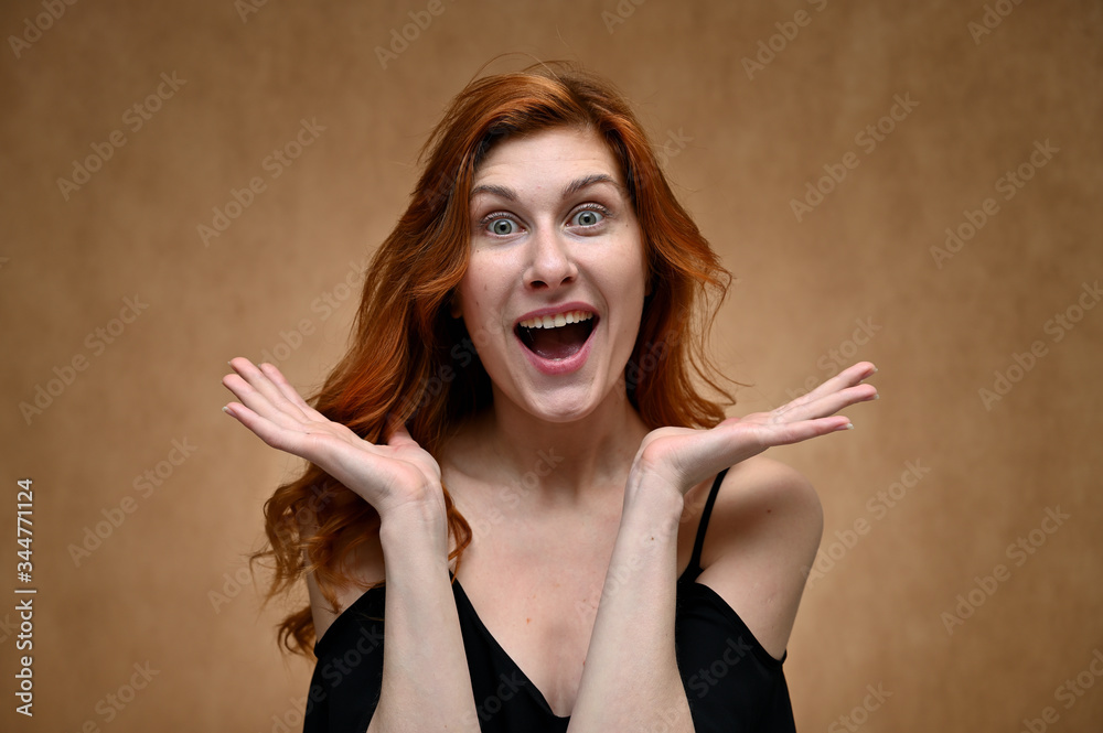 Close-up Portrait of a young pretty woman with a smile with long red hair in a black T-shirt on a beige background. Model joyfully posing.