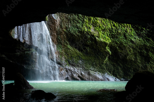A waterfall falls beside a dark cave  pooling in a clear waterfall vault
