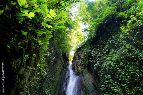 A waterfall falls beside a dark cave  pooling in a clear waterfall vault