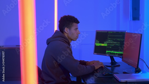 Profile view of african programr working in cyber security center in dark room. He typing something on keyboard. photo