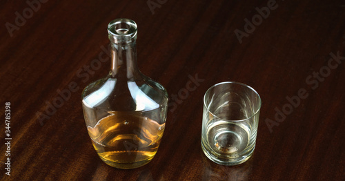 whiskey bottle near transparent glass reflected on brown wooden table at home closeup