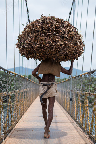 An old Asian man carrying firewood and dried leaves on a suspension bridge 