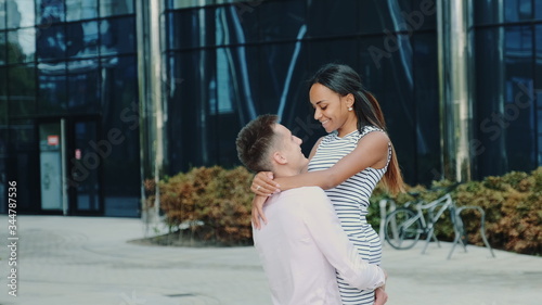 Happy boyfriend holding his black girlfriend in his hands and spinning around outdoors. An office building is in the background.