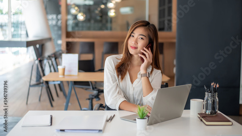 Portrait of beautiful smiling asian female talking on phone in the office.