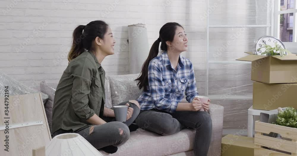 slow motion sweet asian lesbian discussing place furniture for building new family house. two young girls sitting on sofa point out window with urban view look from apartment relax laugh chatting slow motion sweet asian lesbian discussing place furniture for building new family house. two young girls sitting on sofa point out window with urban view look from apartment relax laugh chatting