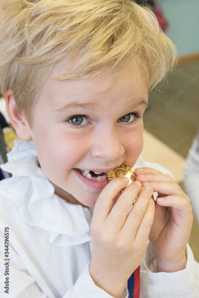 A happy child tries a medal. A beautiful girl tries her gold medal in her teeth. Genuine emotions. The concept of a well-deserved success. A happy child tries a medal. A beautiful girl tries her gold medal in her teeth. Genuine emotions. The concept of a well-deserved success.