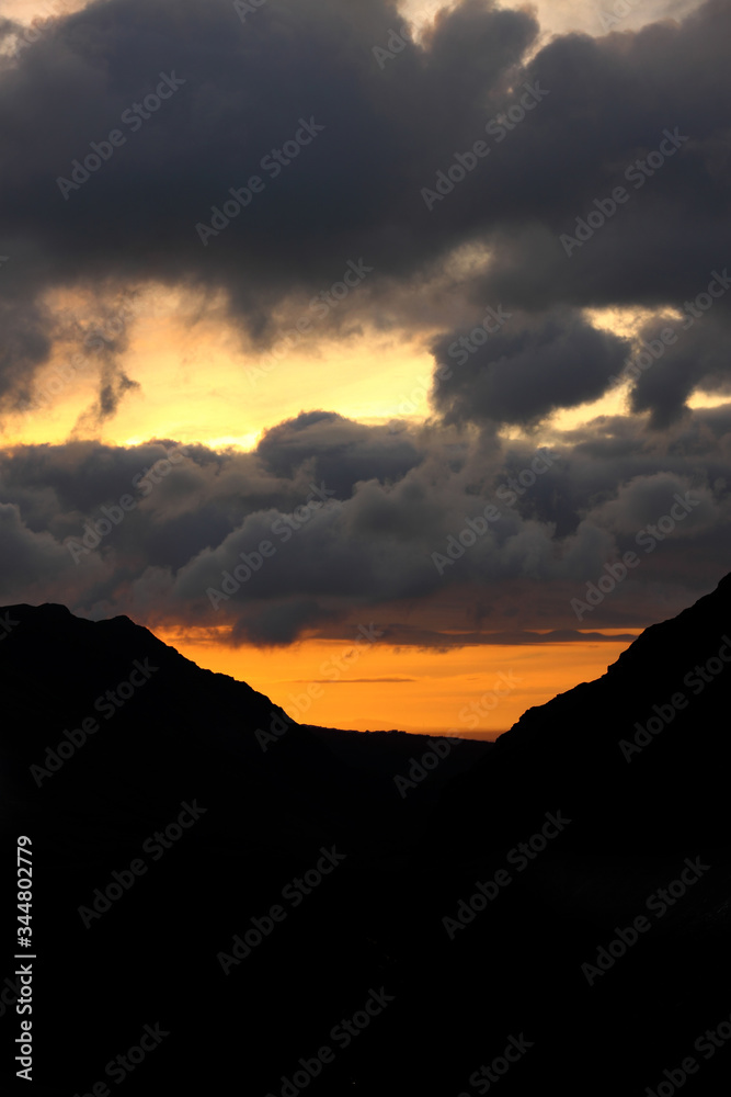 Clouds building at sunset above a valley, with a silhouette of mountains either side Clouds building at sunset above a valley, with a silhouette of mountains either side