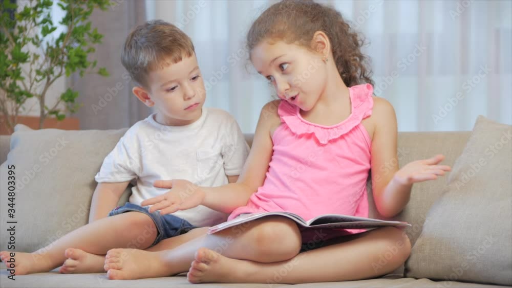 Cute children,sister with a younger brother, looking at a book magazine textbook dictionary tablet read fairy tales, kids are reading books sitting on the couch,preschool and school education. Cute children,sister with a younger brother, looking at a book magazine textbook dictionary tablet read fairy tales, kids are reading books sitting on the couch,preschool and school education.