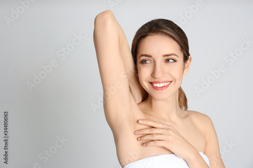 Young woman showing armpit with smooth clean skin on light grey background