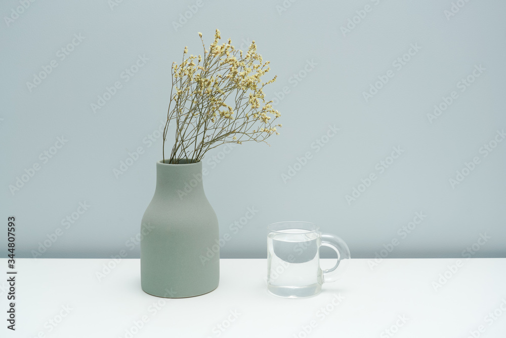 A vase with dried flowers and a glass of water on the white table